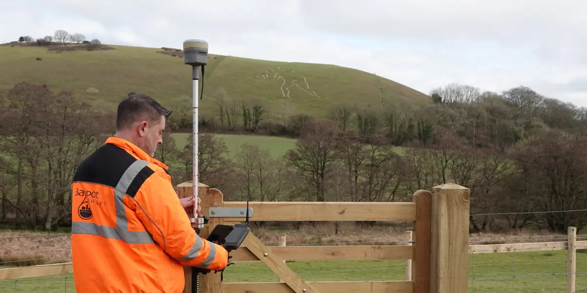 Land surveyor using GPS equipment to conduct measurements near a hill with an ancient hillside carving in the background.