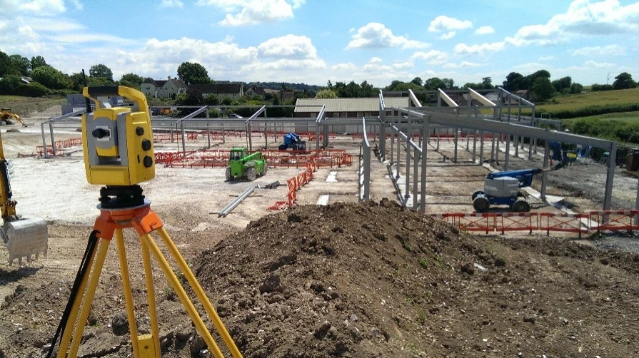 Surveying equipment on a tripod overlooking a construction site with steel framework in progress.