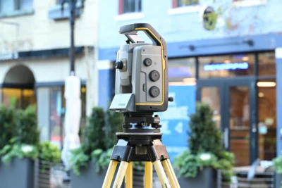 Close-up of a Trimble laser scanning device on a tripod, outdoors in an urban setting.